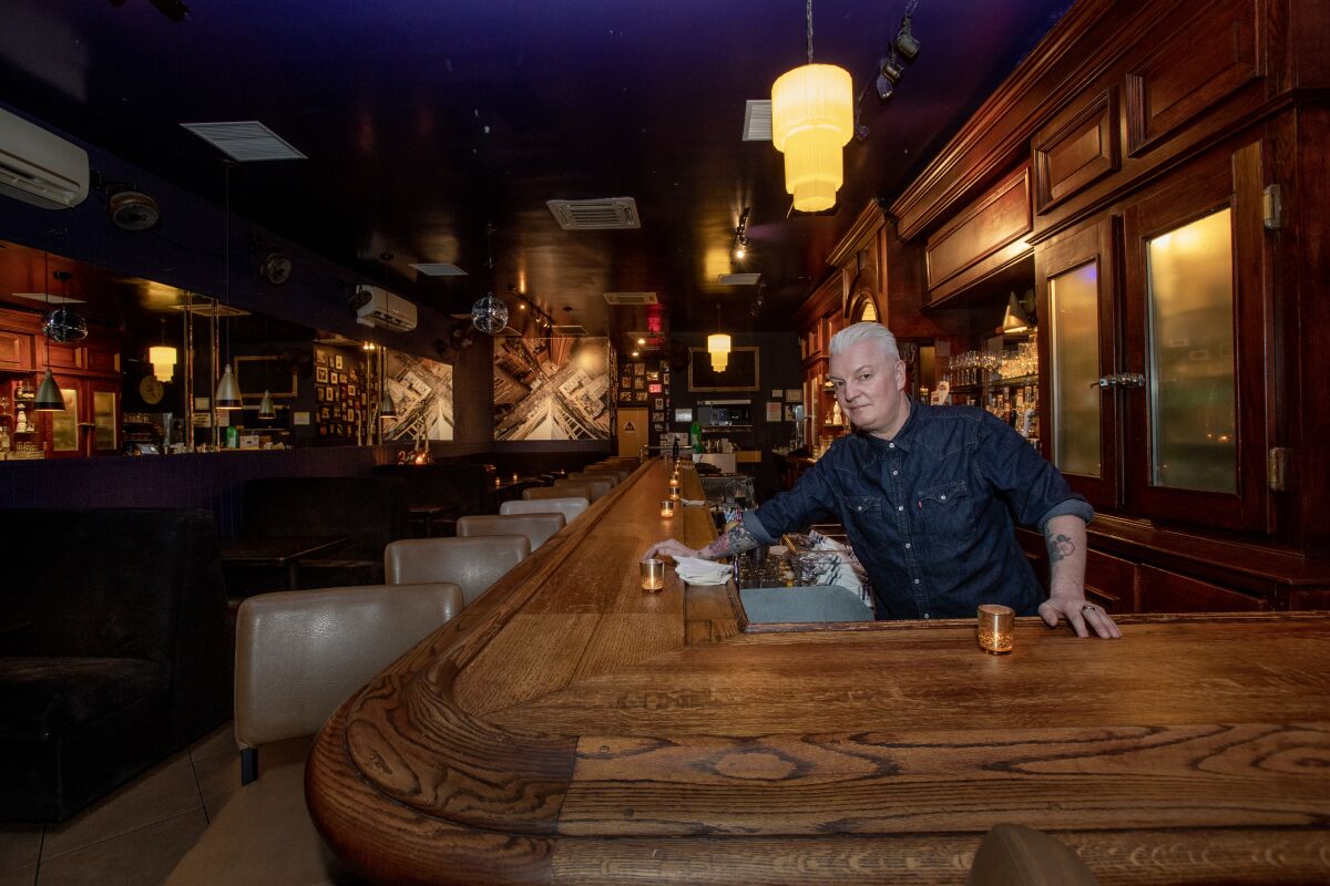 A man stands behind the wooden bar at a restaurant.