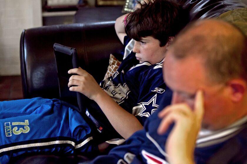 Theo Kennedy, 11, looks at his stats on an iPad while his father, Sean, looks at stats on his iPhone as they watch NFL games on TV.