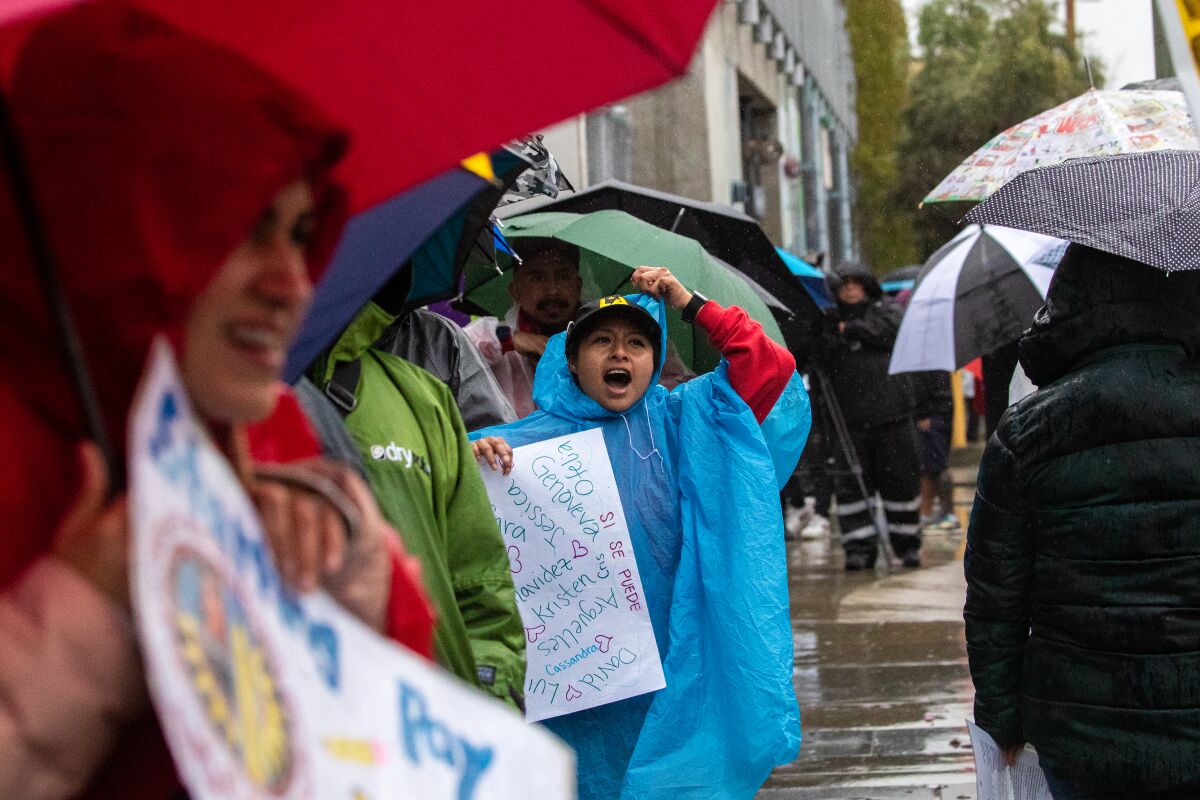 Striking LAUSD employees stand in rain gear in front of a school in Los Angeles