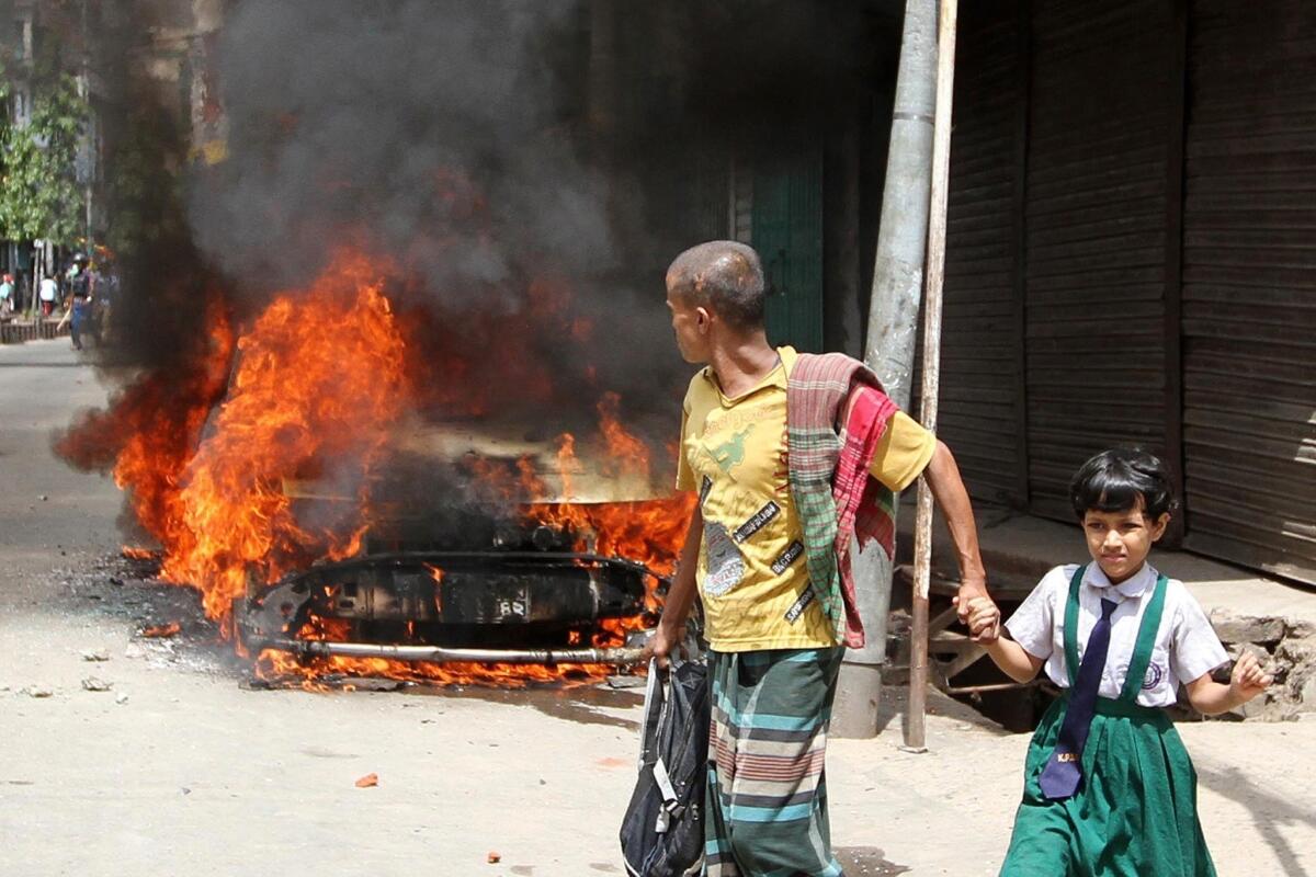 Pedestrians walk past a vehicle set afire during protests of the death sentence handed down against Abdul Quader Molla, a leader of the opposition Jamaat-e-Islami party