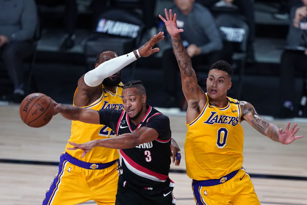Portland Trail Blazers guard CJ McCollum passes between Lakers forward LeBron James, left, and forward Kyle Kuzma.