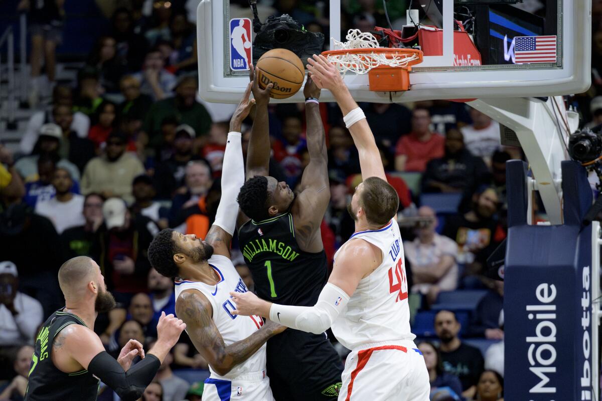 Clippers forward Paul George, left, and center Ivica Zubac, right, try to stop Pelicans forward Zion Williamson from scoring.