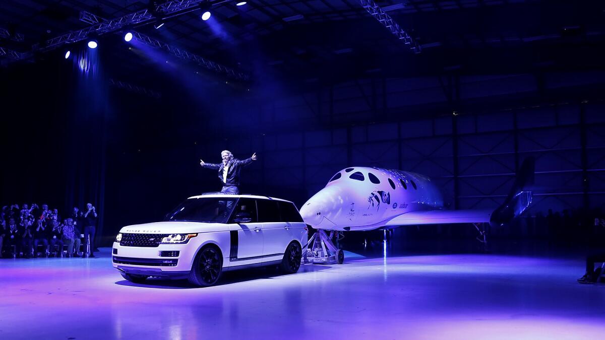 Richard Branson stands in an SUV as it tows the new Virgin Galactic SpaceShipTwo, named VSS Unity, at an unveiling event at the Mojave Air and Space Port Friday. The new vehicle replaces the company's previous SpaceShipTwo, which broke apart in midair nearly 16 months ago, killing one of two pilots.