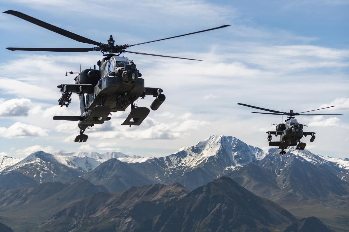 Two military helicopters fly with a mountain range in the background