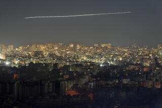 A timed-exposure image shows the contrail of a jet airliner flying over Beirut through smoke from Israeli airstrikes
