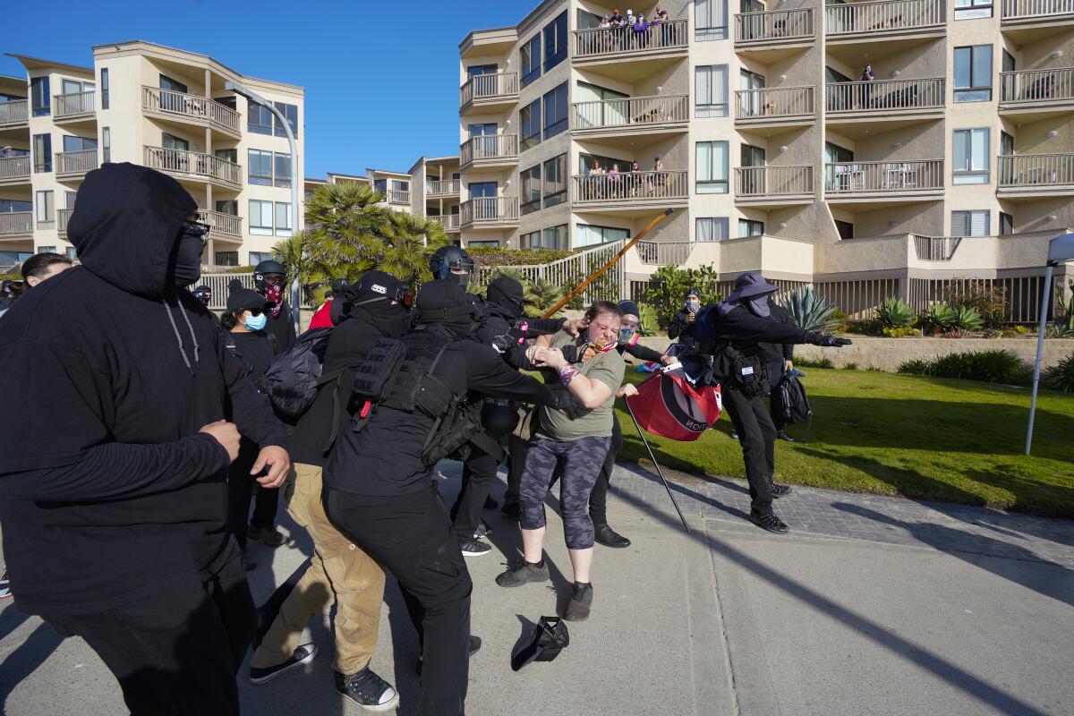 Black-clad counterprotesters fight a woman on the boardwalk near Crystal Pier in Pacific Beach during pro-Trump Patriot March