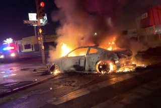 Flames engulf a car on a city street after dark.