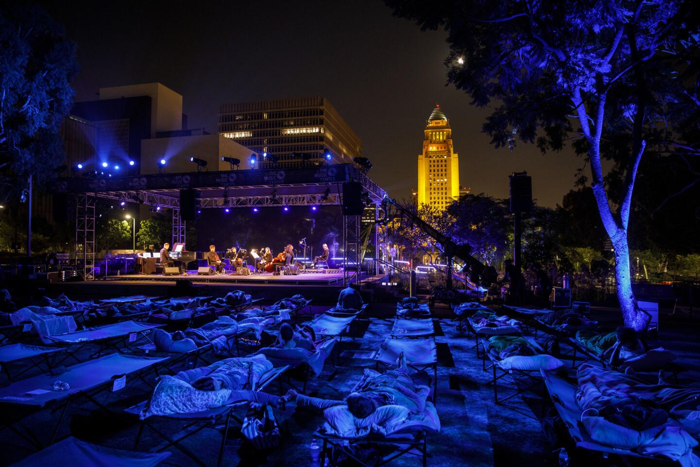 Max Richter performs "Sleep" as people lie in cots during a performance in Grand Park on Saturday, while L.A. City Hall is illuminated in gold to honor the late Los Angeles Times food critic Jonathan Gold.
