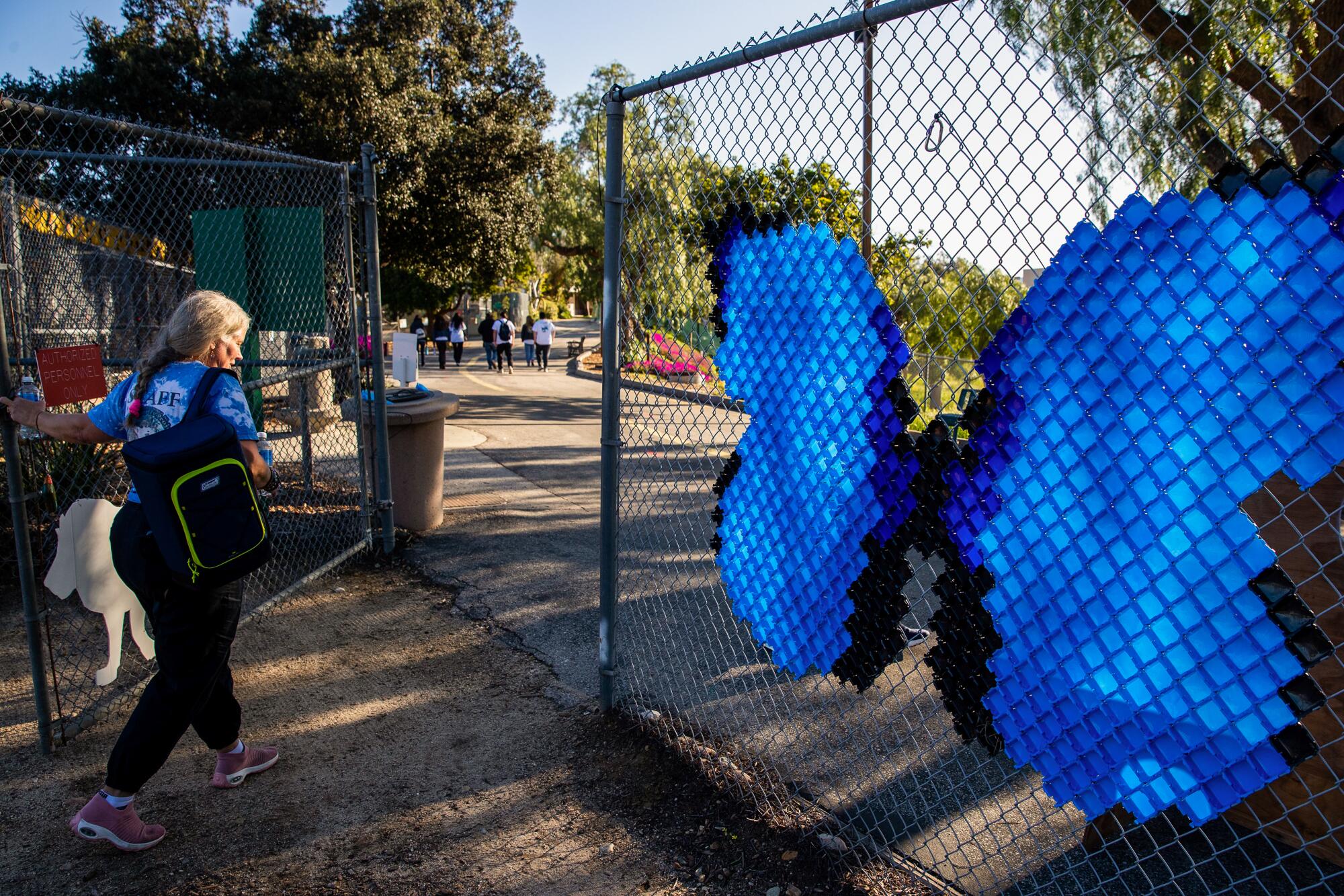 A woman stands near a chain-link gate containing a sign in the shape of a large blue butterfly.