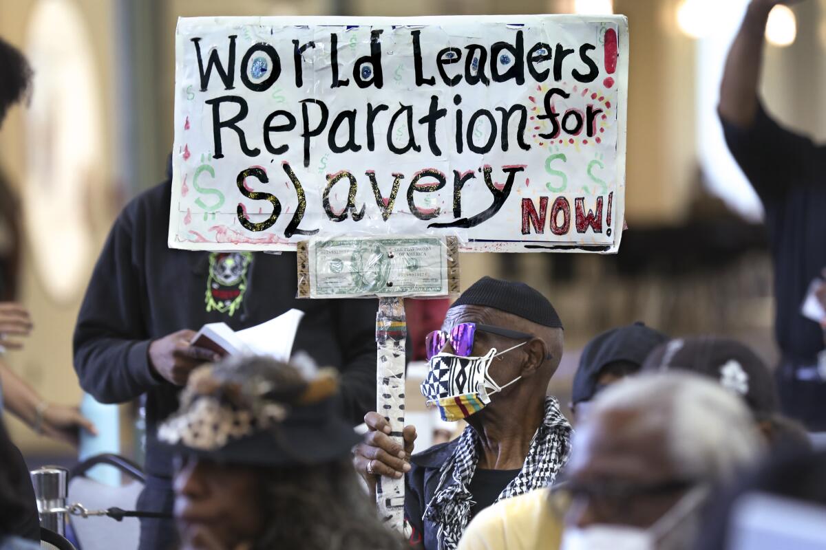 Los Angeles resident Walter Foster holds up a sign as the California Reparations Task Force meets to hear public input.