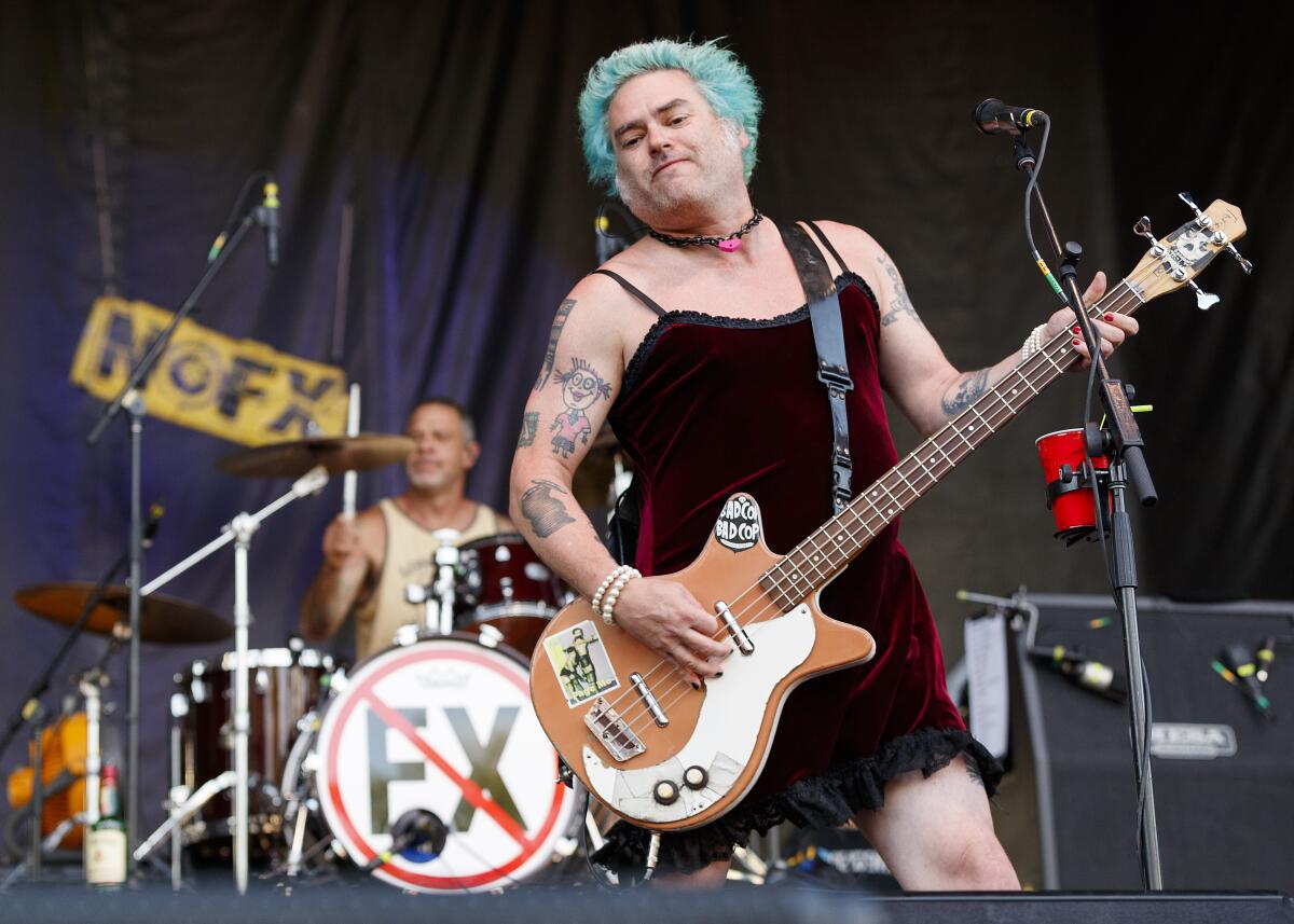 A man with blue hair wearing a dress plays the bass on stage while another man drums behind him