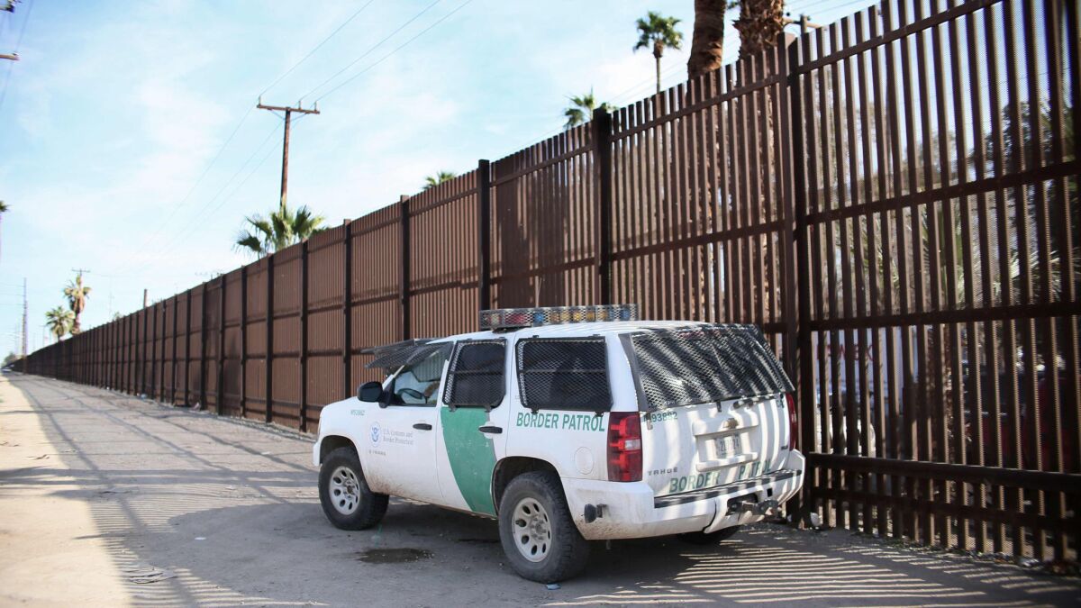 A Border Patrol agent looks over the wall in Calexico. A barrier built in the 1990s from recycled metal scraps and landing mat will be torn down for bollard-style posts that are 30 feet high.