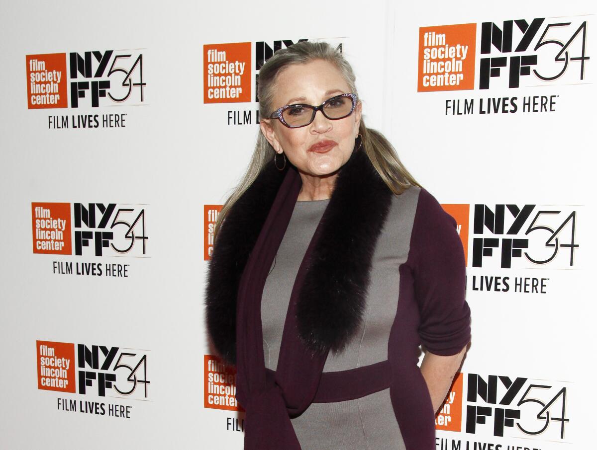 Carrie Fisher wearing tinted glasses, a purple and gray dress, and a furry scarf
