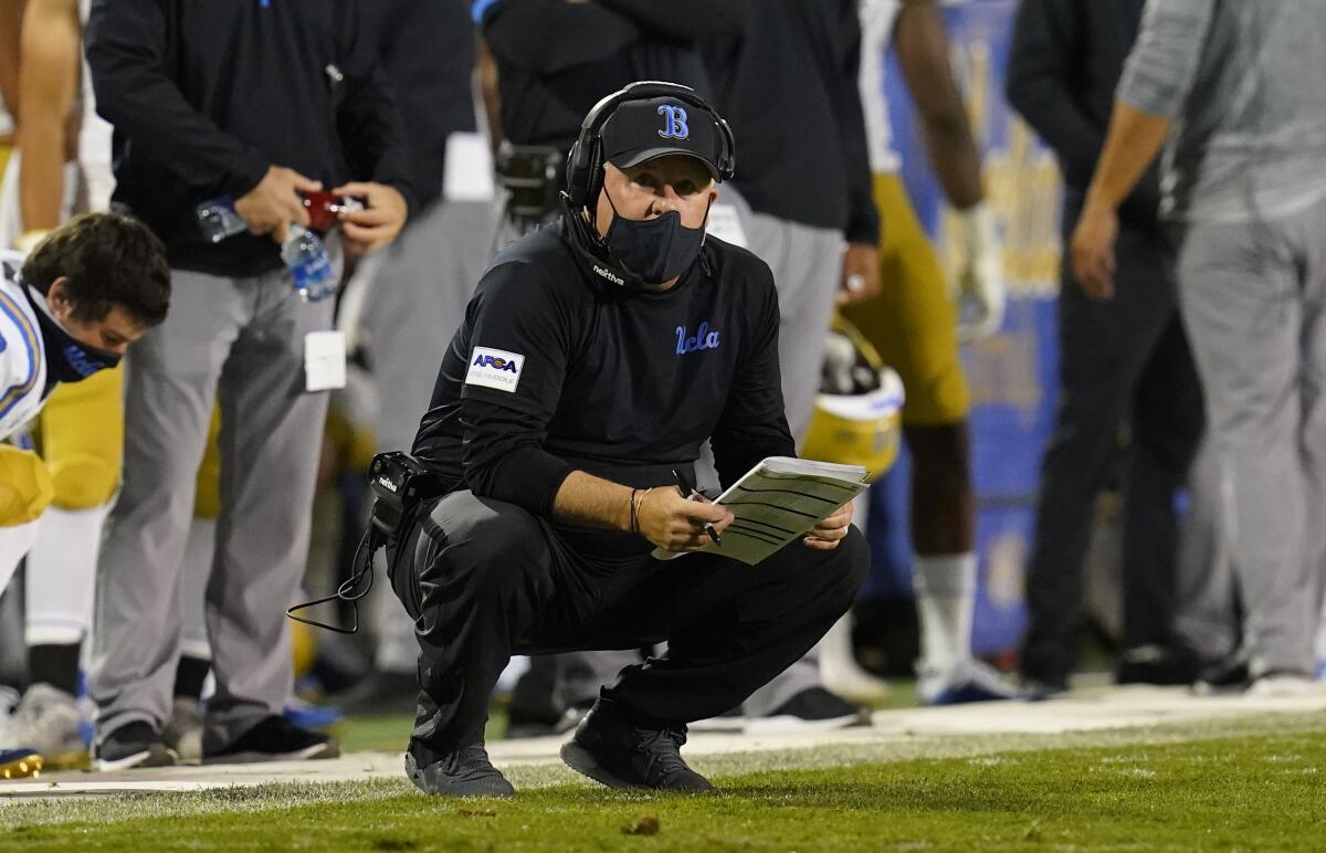 Chip Kelly crouches on the sideline as he coaches UCLA in a game against Colorado.