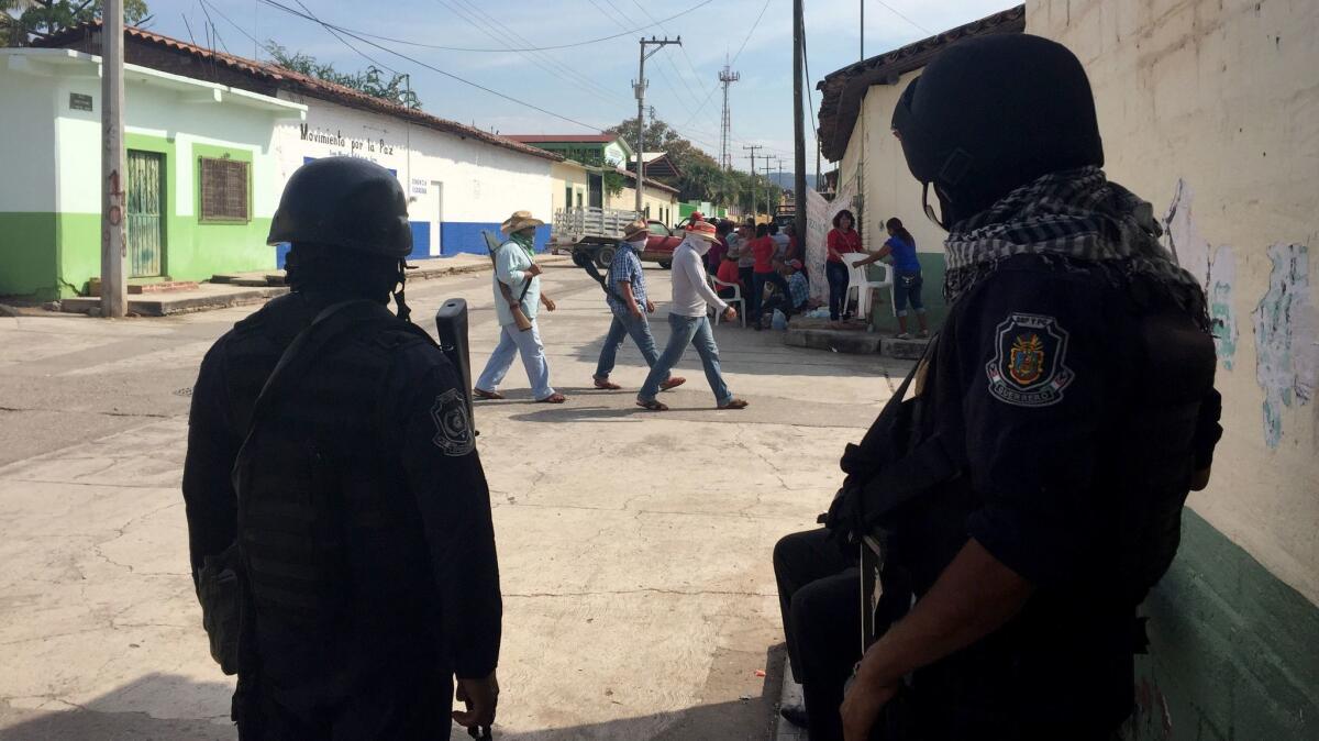 Local vigilantes who call themselves a "self-defense force" walk past police officers in San Miguel Totolapan.