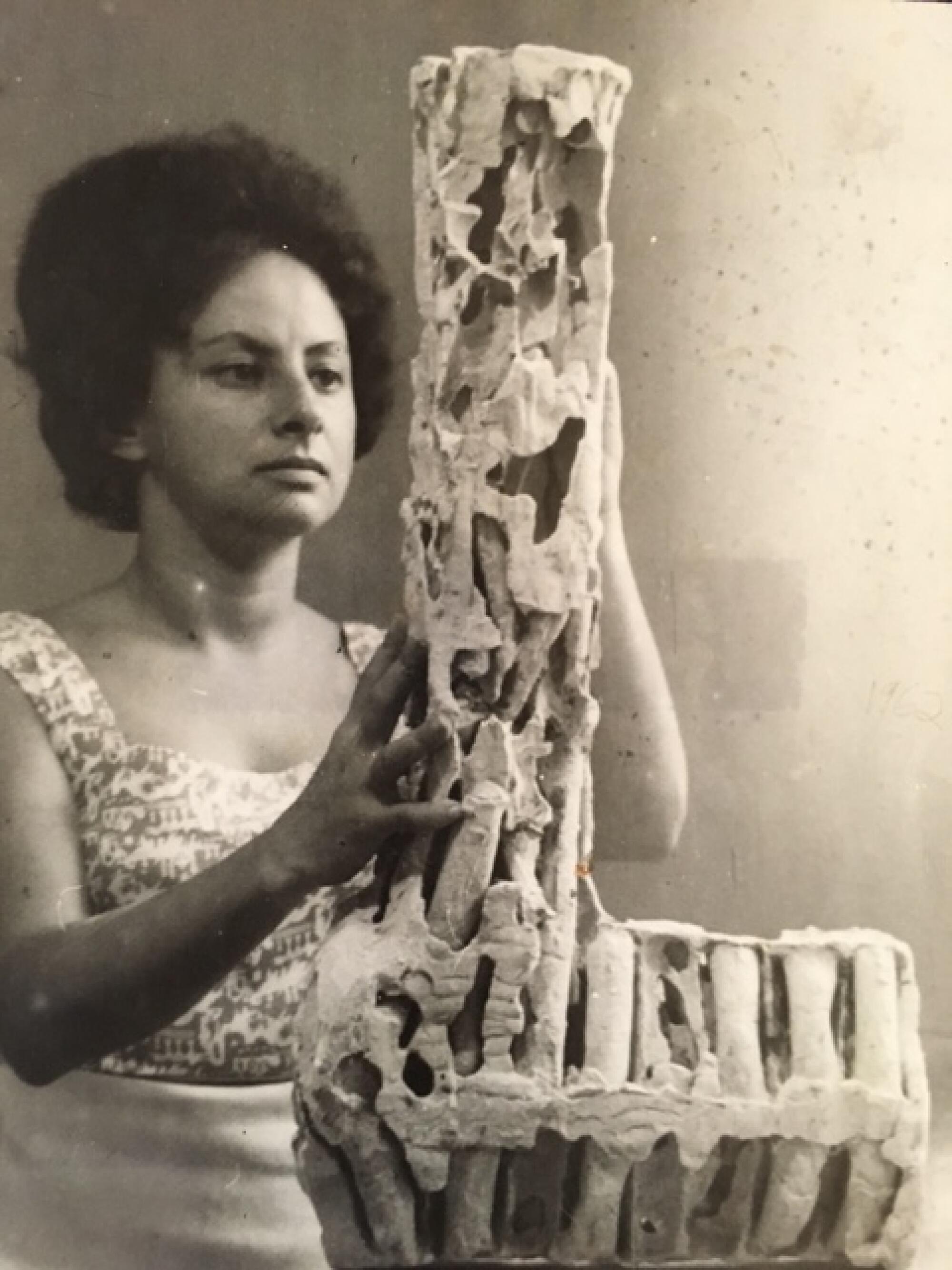 A young woman cradles a sculptural tower in her hands.  