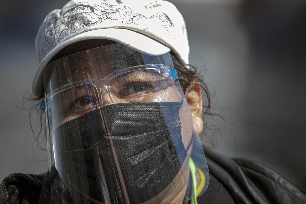 A woman wears a hat, face shield and a mask.
