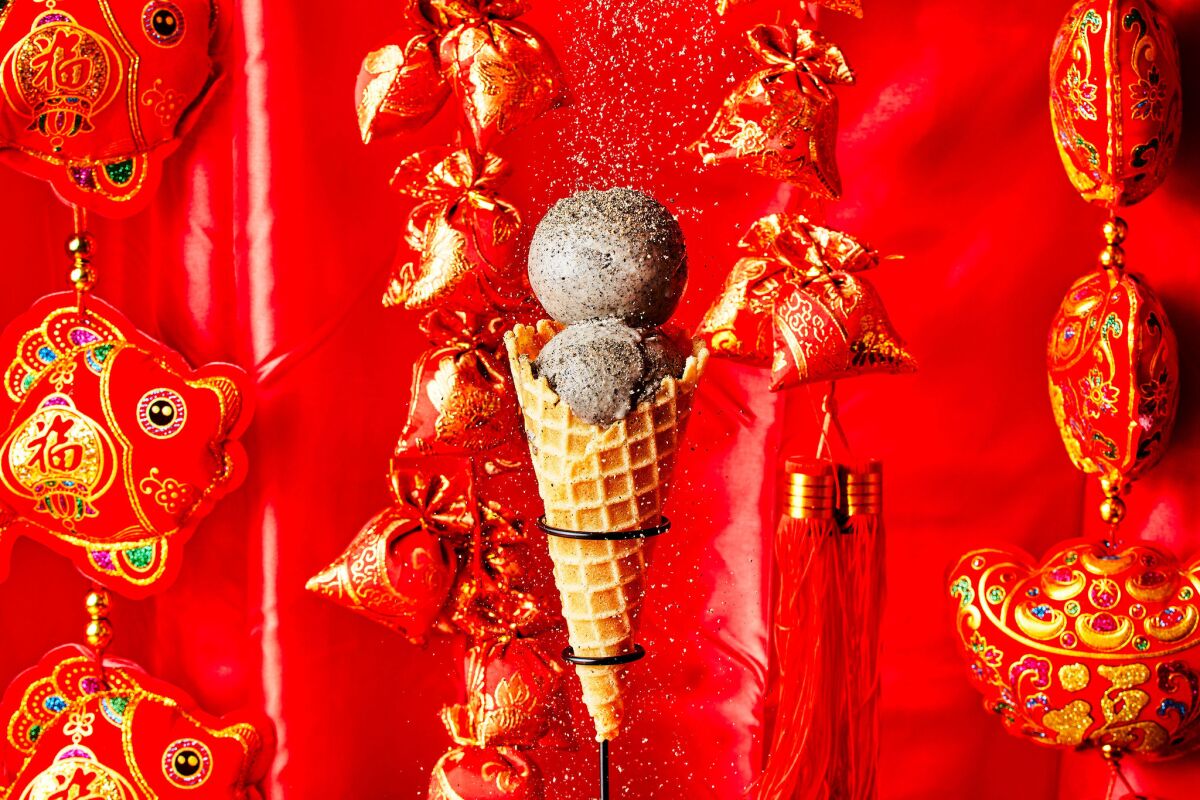 A shot of Dear Bella Creamery's black sesame ice cream, scooped into a cone, sitting against a festive red and gold backdrop