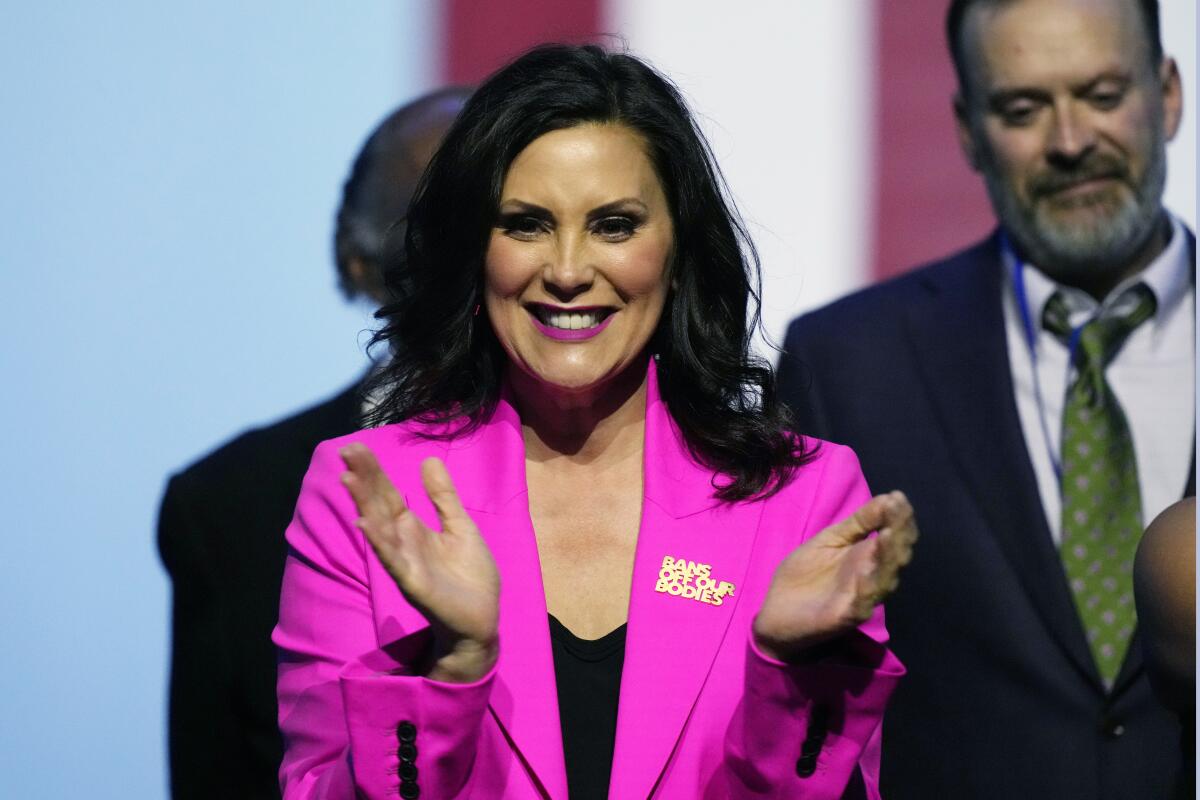 A smiling woman with dark hair, wearing a deep pink jacket and a pin that says "Bans off our bodies," applauds