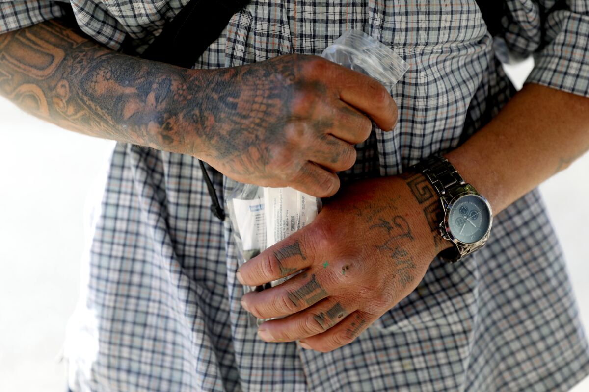 A man, seen in his midsection -- his hands and arms tattooed -- holds a plastic bag with a naloxone kit.