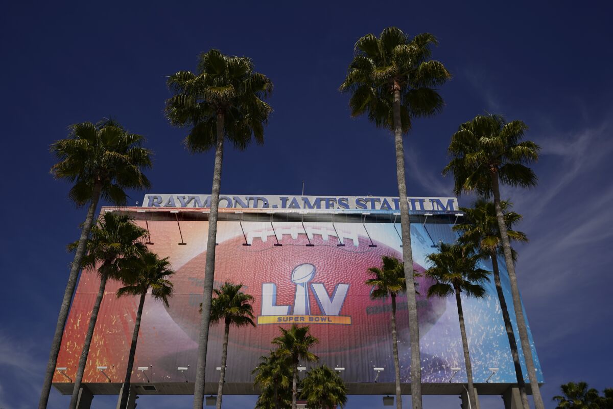A stadium sign for Super Bowl 55 is framed by palm trees.