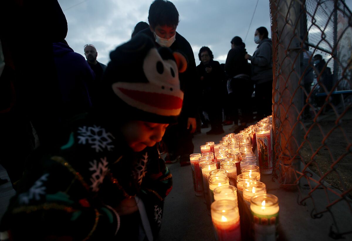 A child kneels next to rows of candles set up next to a school fence