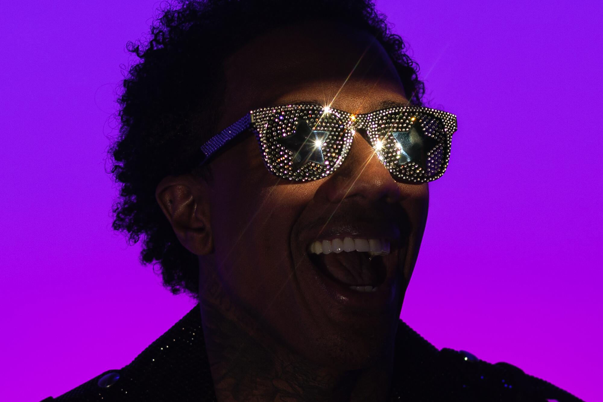 Backed by a glowing purple backdrop, Nick Cannon poses for a portrait in sparkly shades.