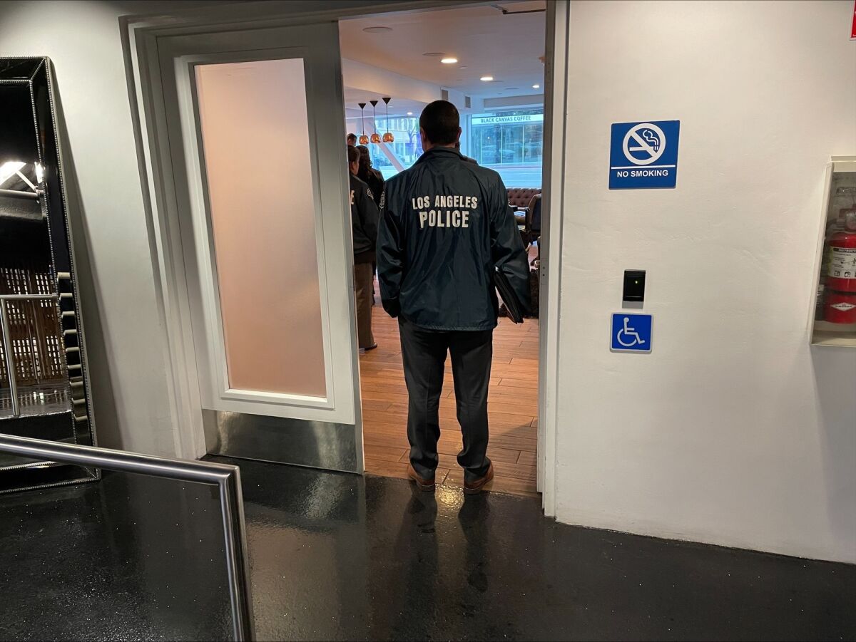 A man wearing an LAPD jacket stands in a doorway.