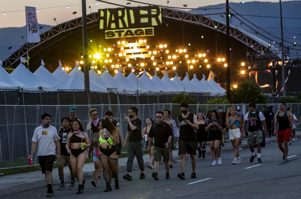 Crowds of festival-goers, only a few wearing wearing masks, walk to the entrance to the Hard Summer music festival