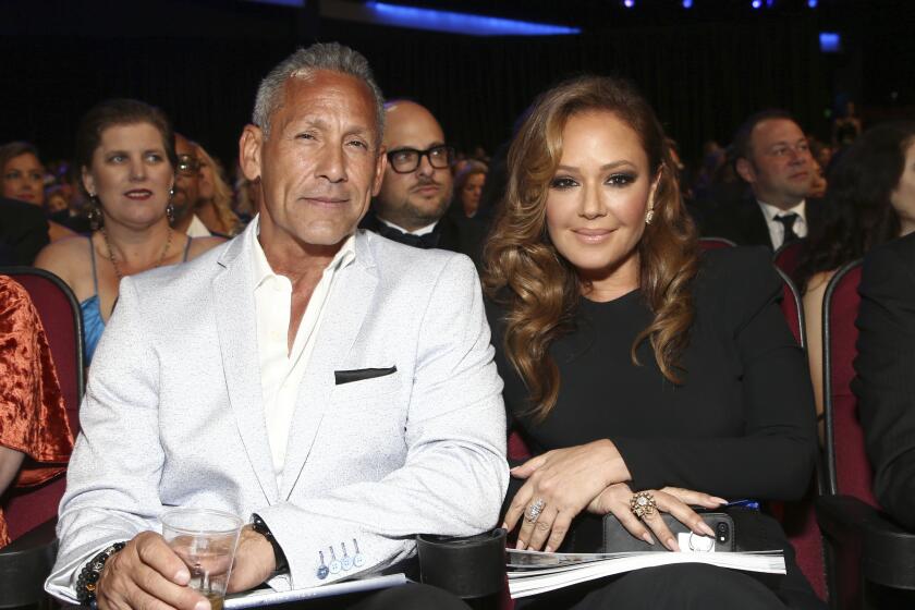 Angelo Pagan in a tuxedo holds a drink while seated next to wife Leah Remini inside a theater