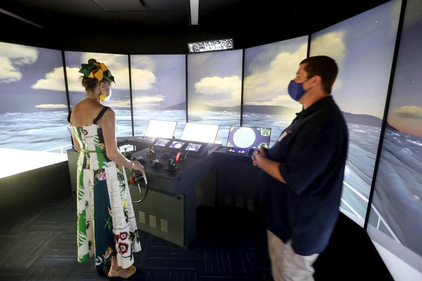Mary Lynn Bergman-Rallis, left, takes the steering wheel of the new full bridge simulator which simulates arriving at the Avalon Harbor on Catalina Island during the Orange Coast College Professional Mariner Training Center dedication center on Friday. The simulator can replicate situations from calm sunny days to major storms.