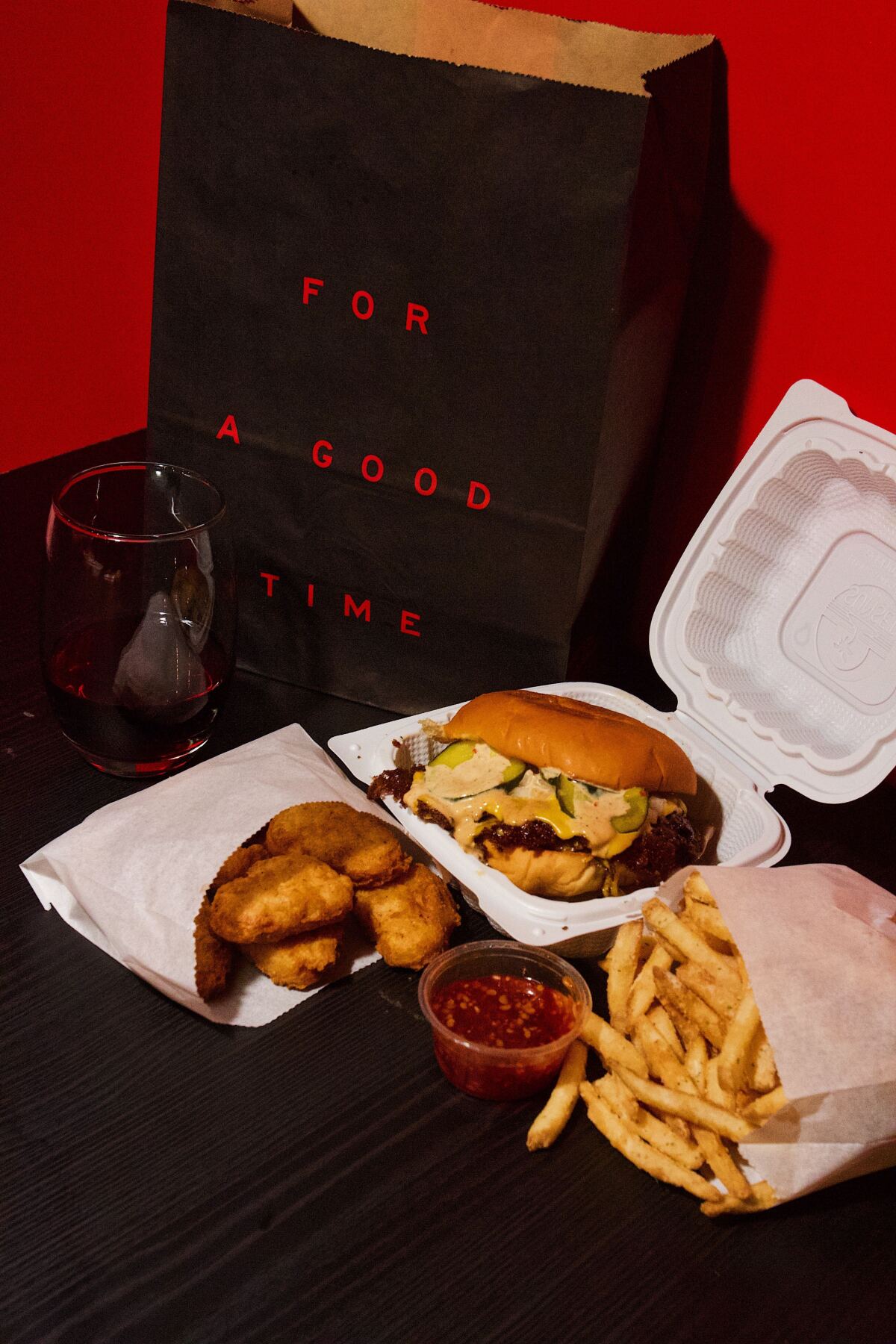 A cheeseburger, chicken nuggets, bag of fries and glass of red wine.