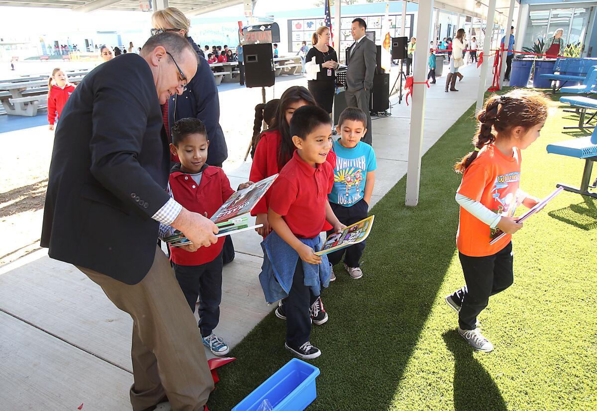 Whittier Elementary school principal Scott Wilcox hands out books during the debut of Zelda's Corner, a new reading program named after the principal's service dog, where kids can gather at the corner of the playground and read books.