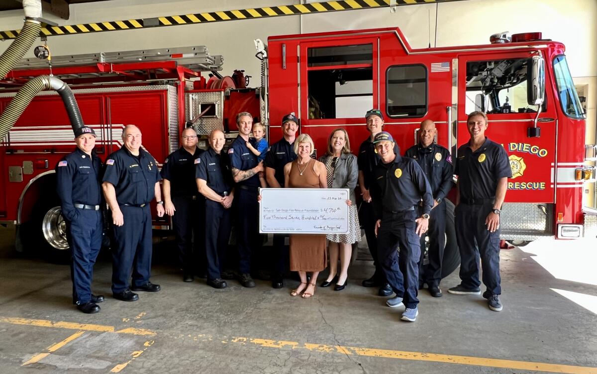 Margie Lord (in brown dress) presents a check for $4,700 donated by her friends to the San Diego Fire-Rescue Department.