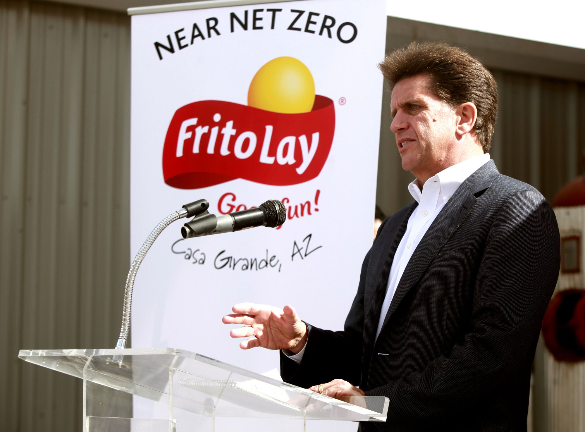 Al Carey speaks at a lectern in front of a sign with Frito-Lay's logo that says Near net zero