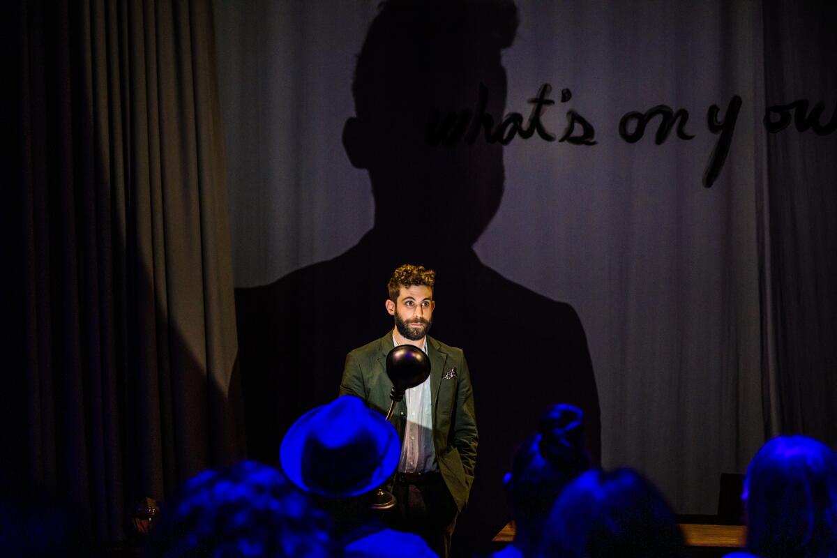 A lone man speaks into a mic onstage 