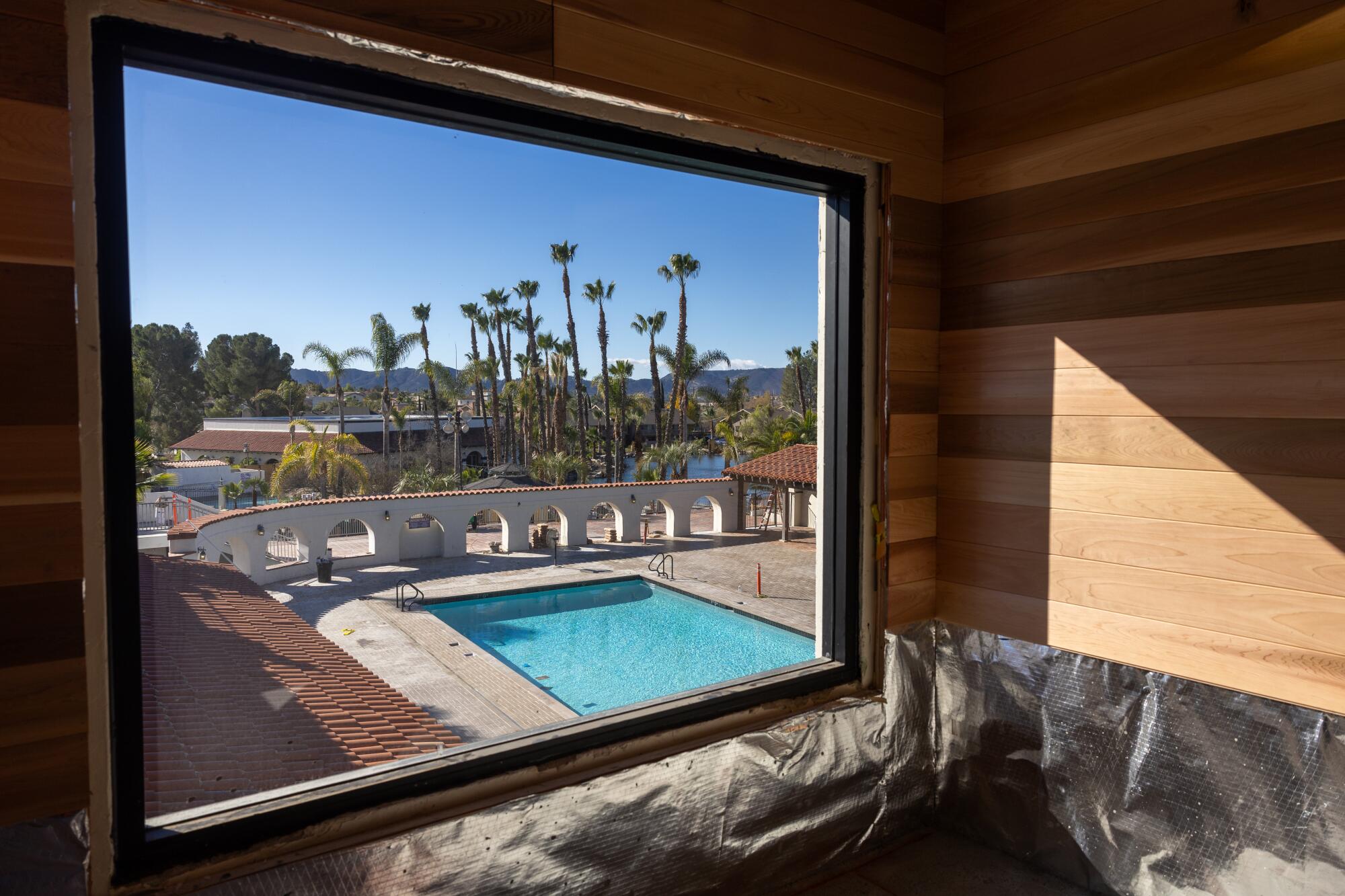 From a sauna under construction you look out onto a swimming pool with a row of palm trees behind it.