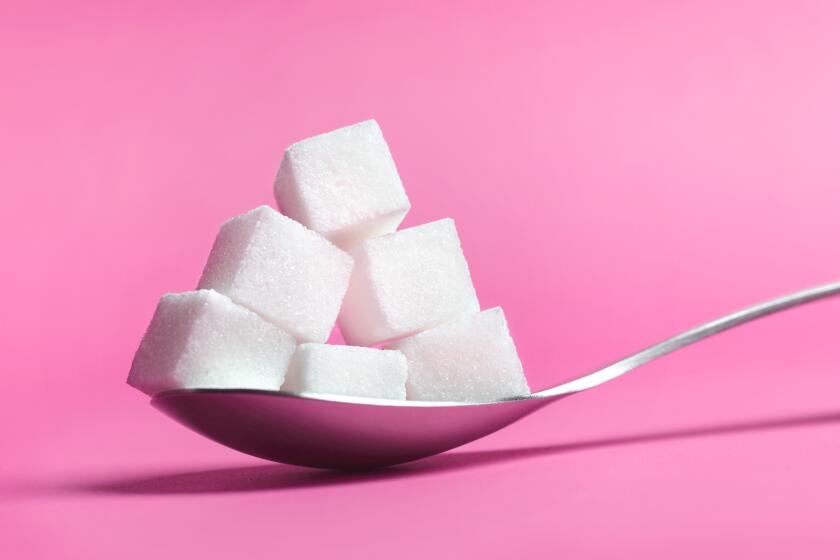 Close up of a spoon pilled high with sugar cubes on pink background