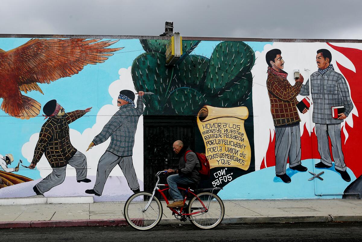 A man on a bicycle passes by a mural of gang members fighting and making peace in the Wilmington neighborhood.