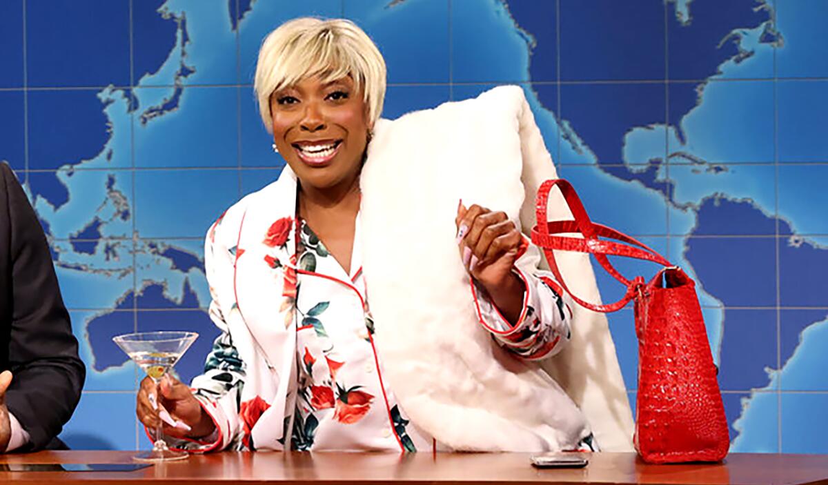 Still from "Saturday Night Live" shows Michael Che and Ego Nwodim, wearing fur and a blond wig, sitting at an anchor's desk.