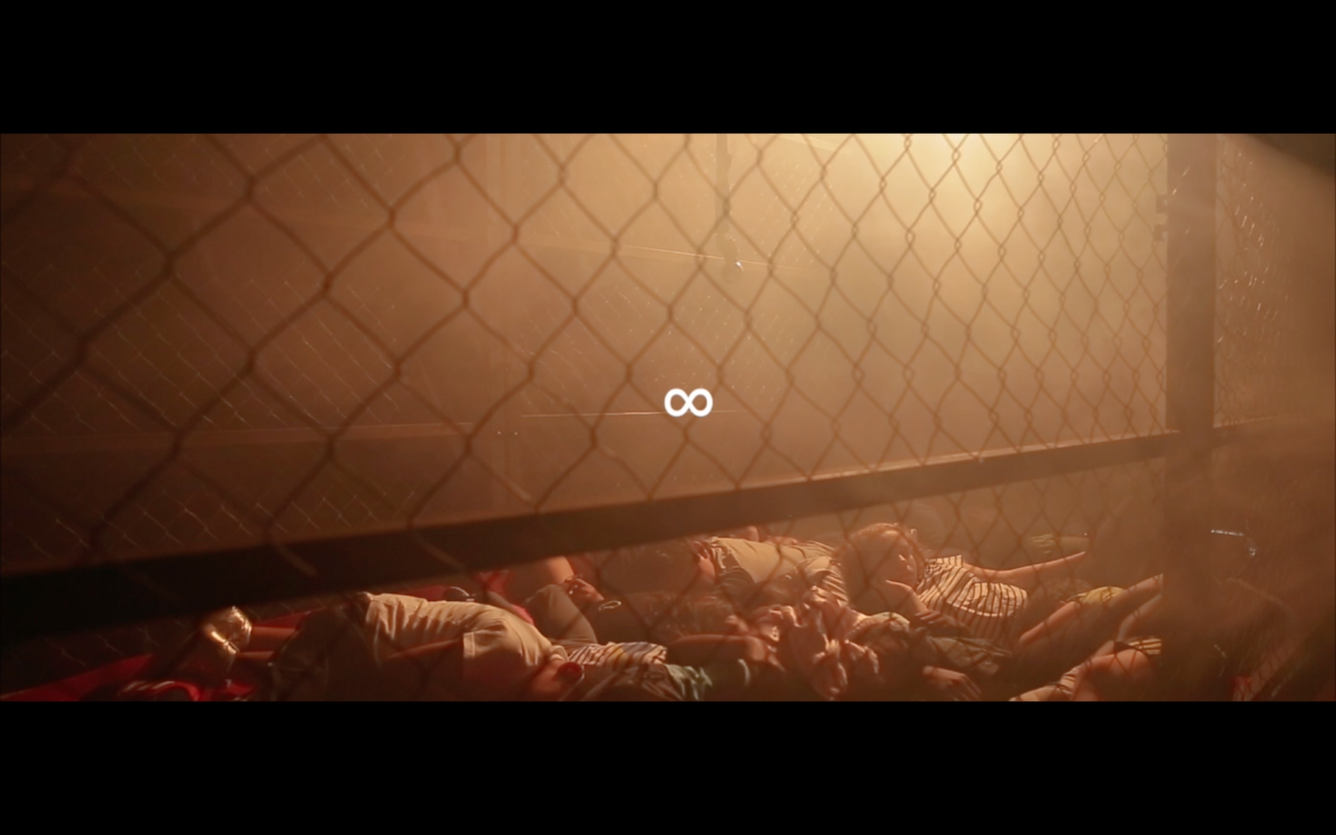 A film still shows a group of children lying down in a cage in a smoky penumbre.