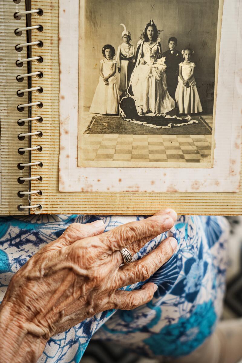 An aged hand holds up a photo album open to a photo of a young woman crowned "vanilla queen"