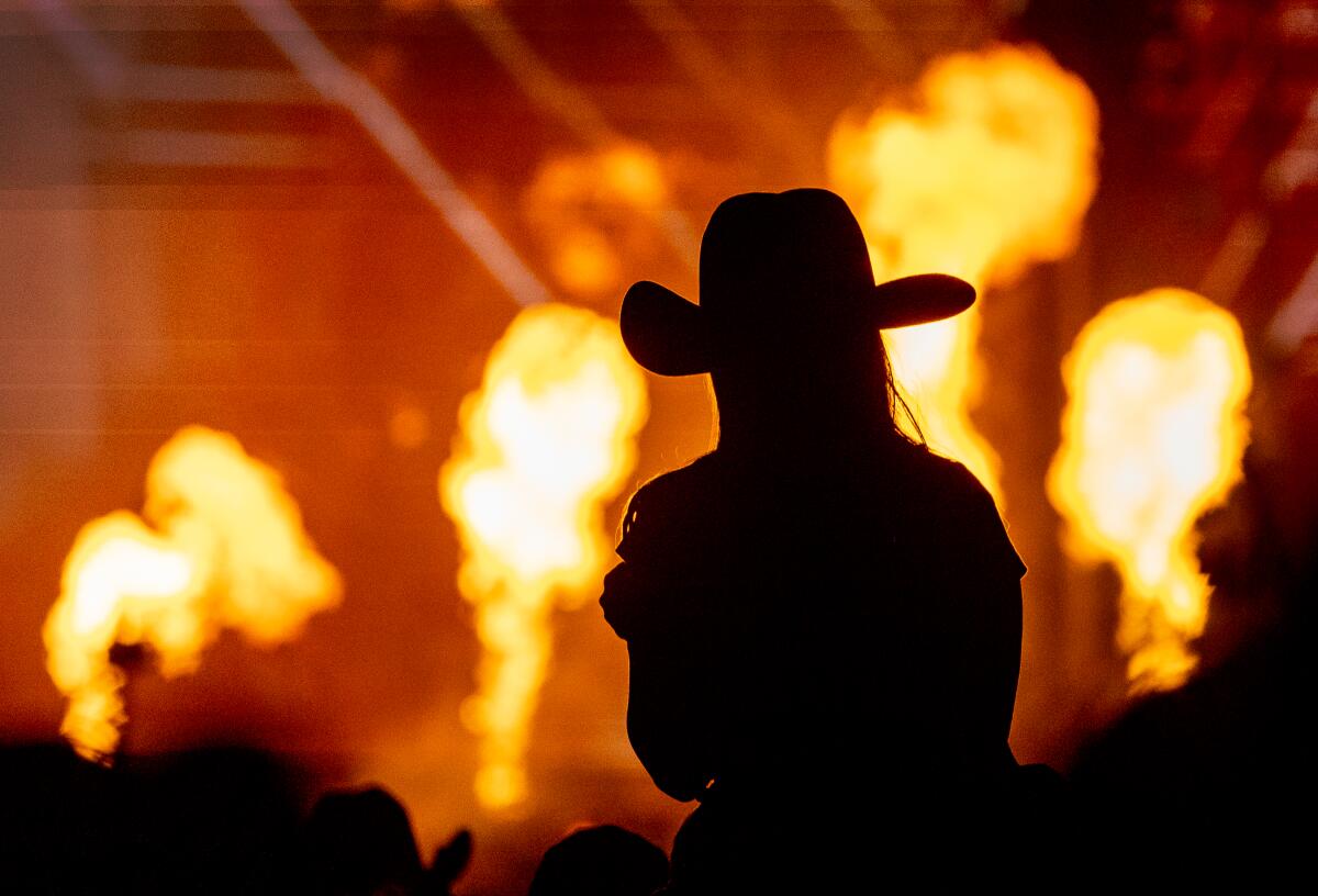 Silhouette of a woman with a cowboy hat in front of a fireworks show 