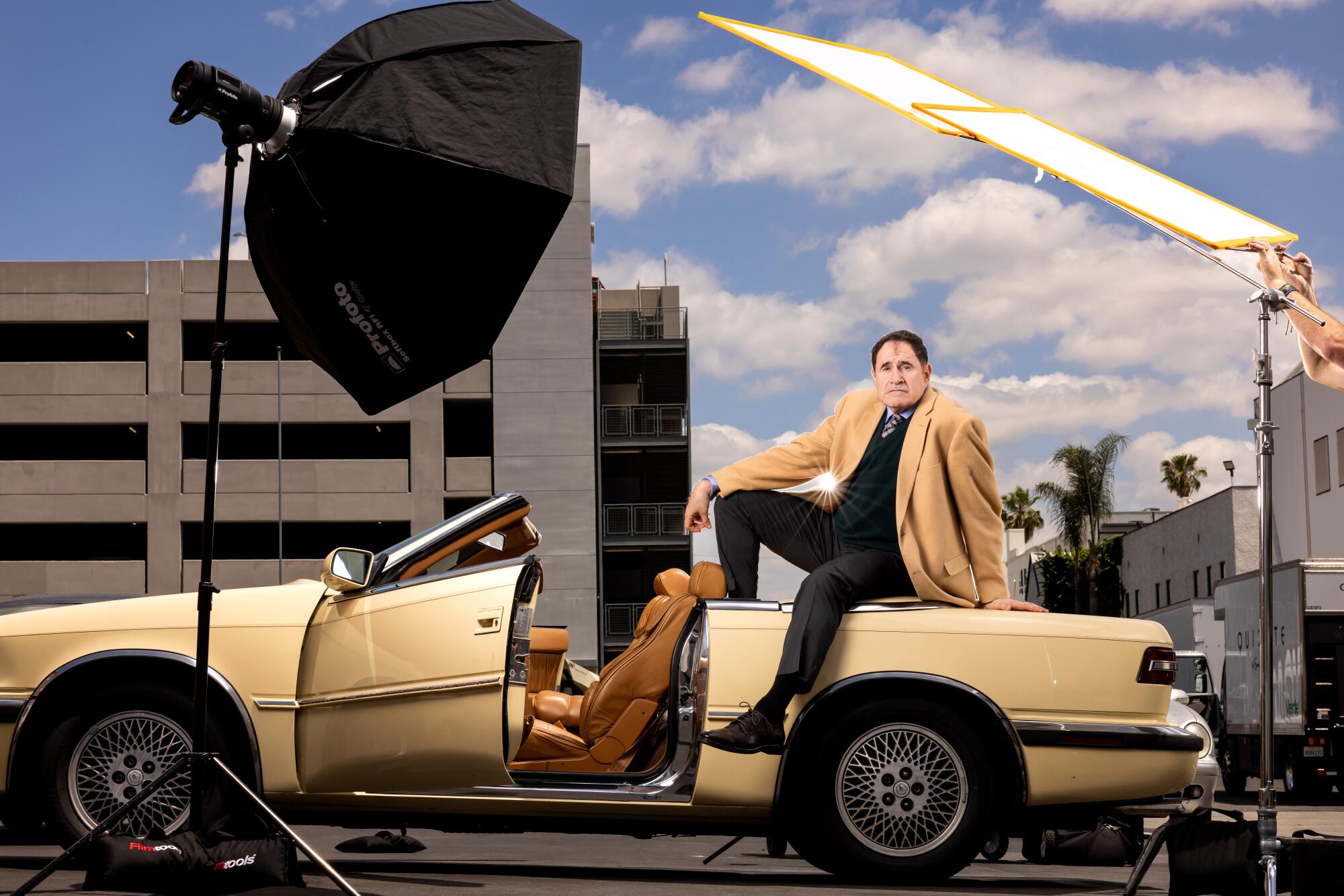 A man sits atop a butter yellow convertible on a studio lot.