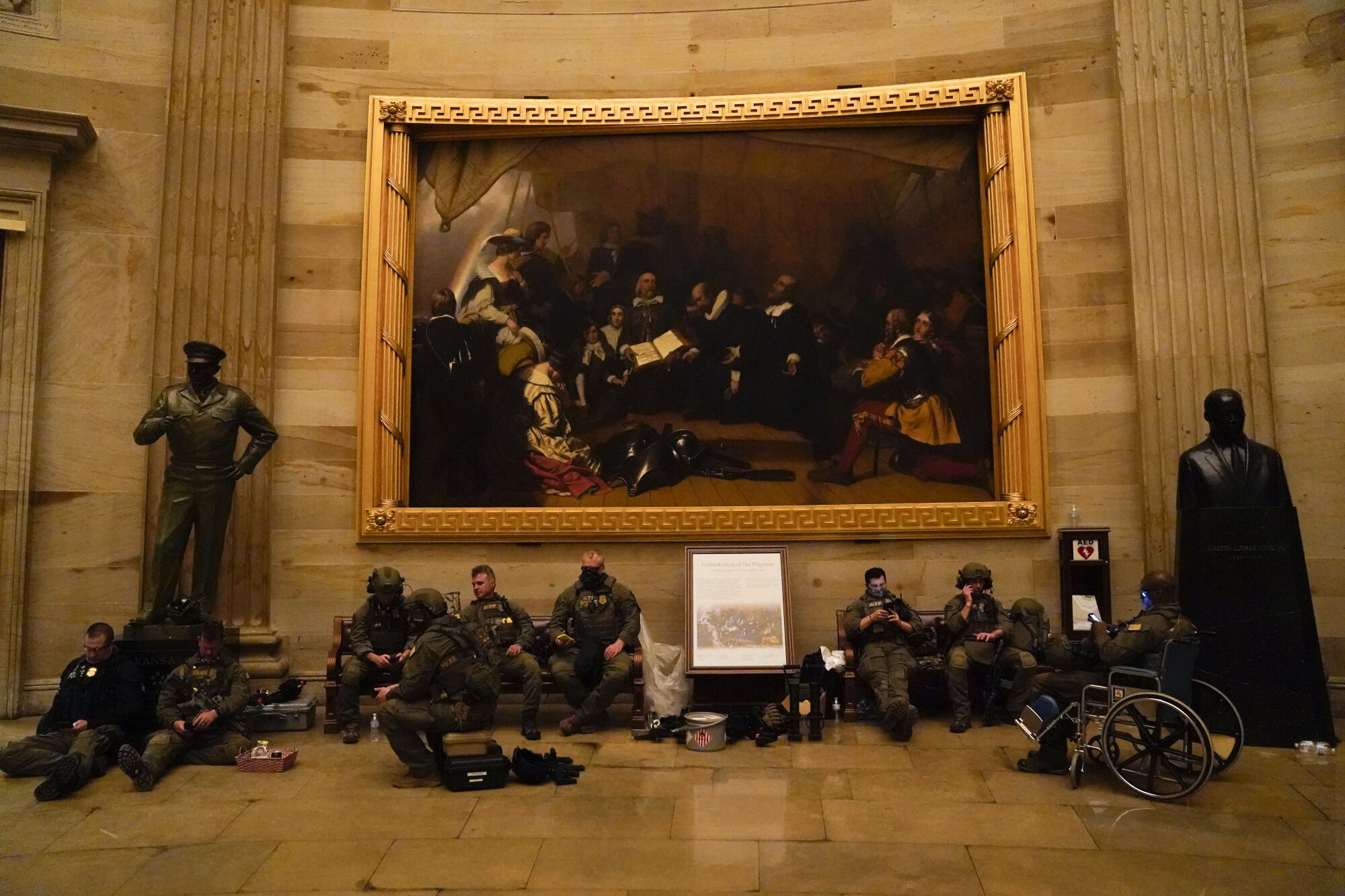 Capitol police rest, sitting on benches and the floor, one in a wheelchair, outside the House chamber.