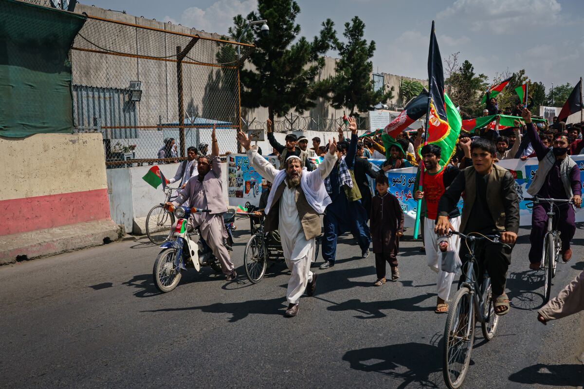 People on foot and on bicycles march down a street carrying red, black and green flags 