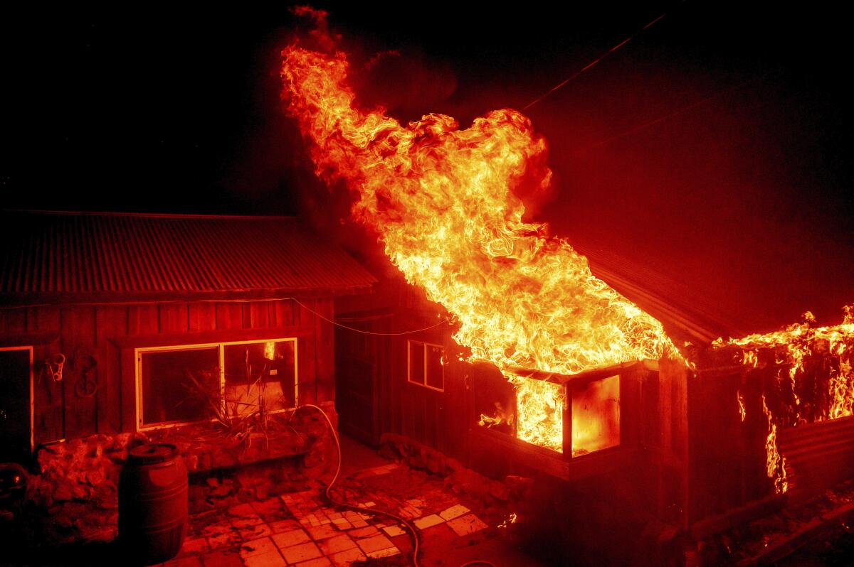 Flames shoot from the window of a one-story home in the middle of the night, casting a red glow