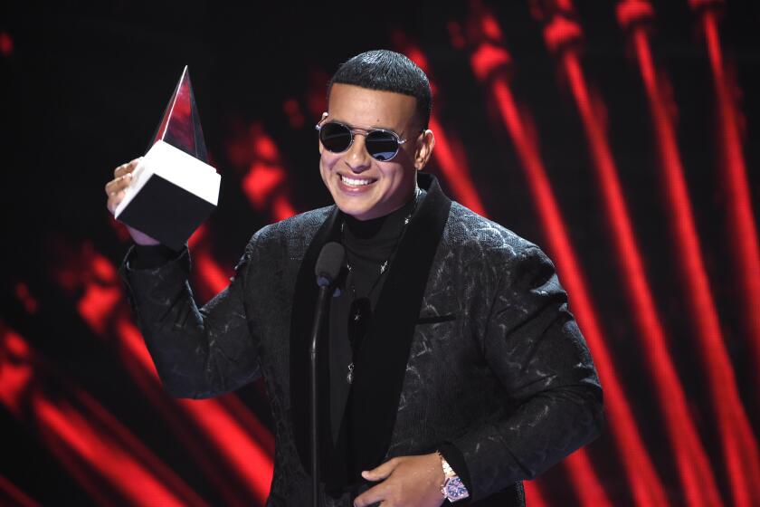A man wearing a suit and sunglasses hold up a music trophy