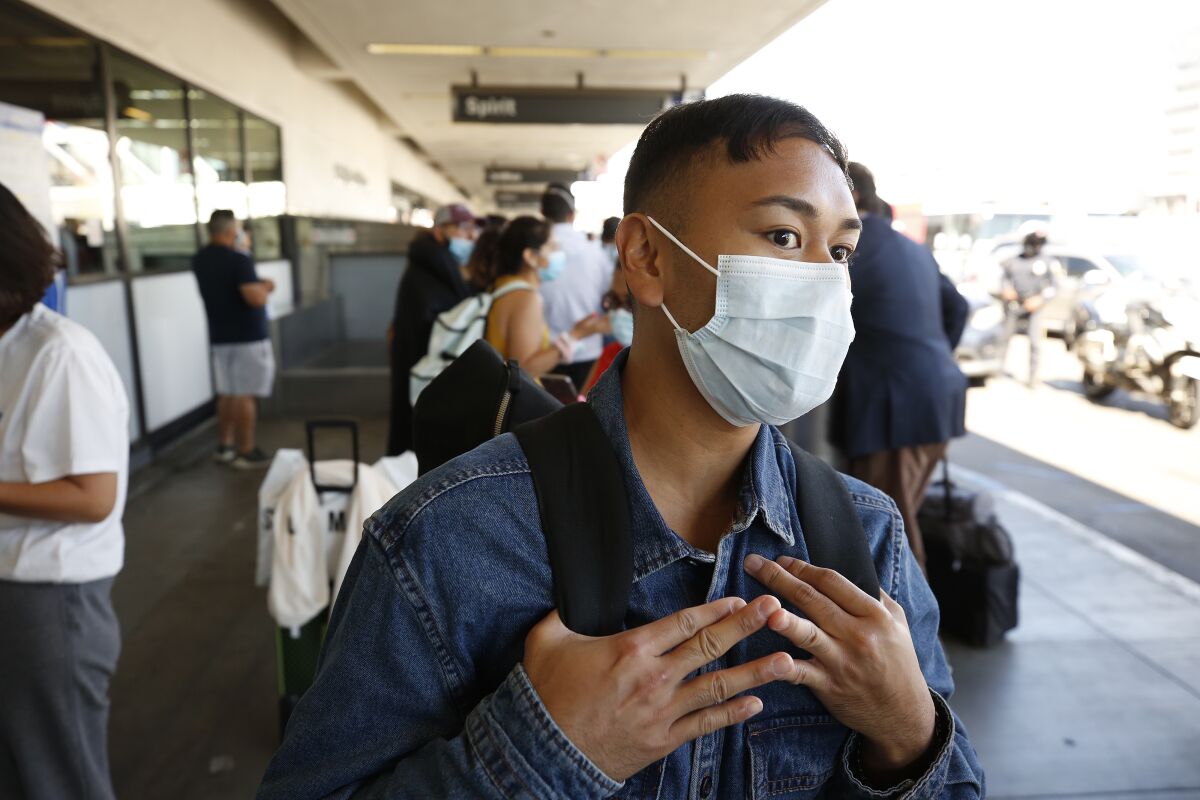 A man wearing a masks waits outside at the airport
