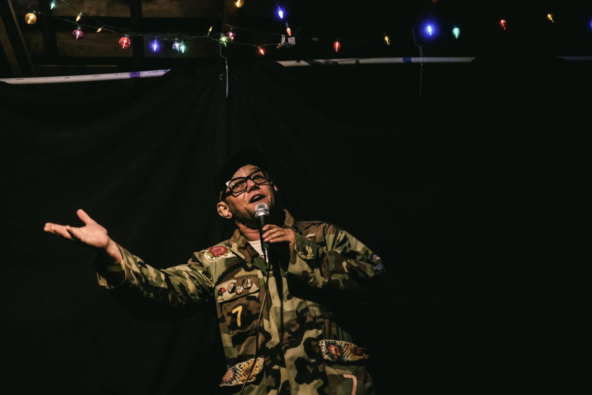 A comedian performs wearing a camouflage jacket.